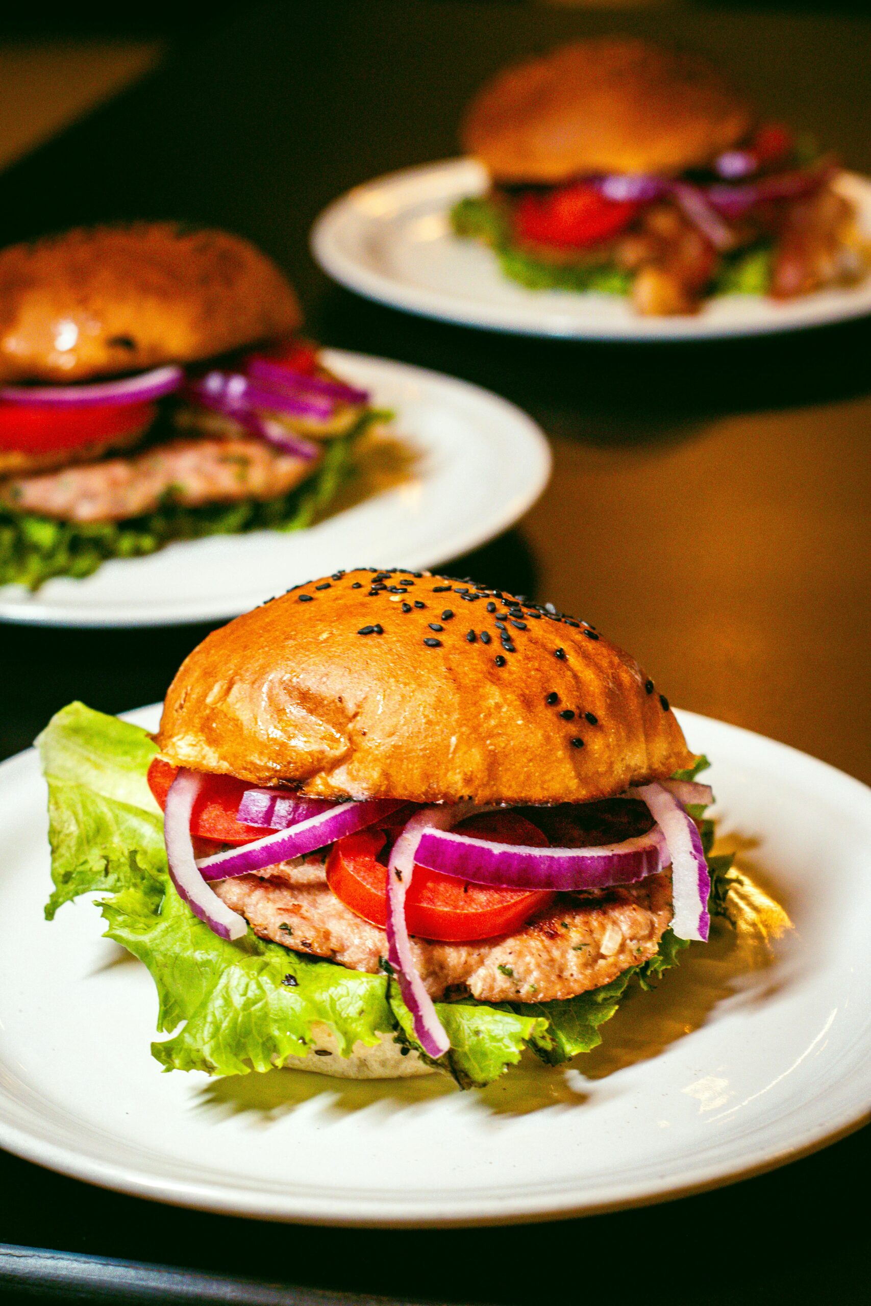 Appetizing gourmet burgers featuring fresh lettuce, tomatoes, and onions on sesame buns.