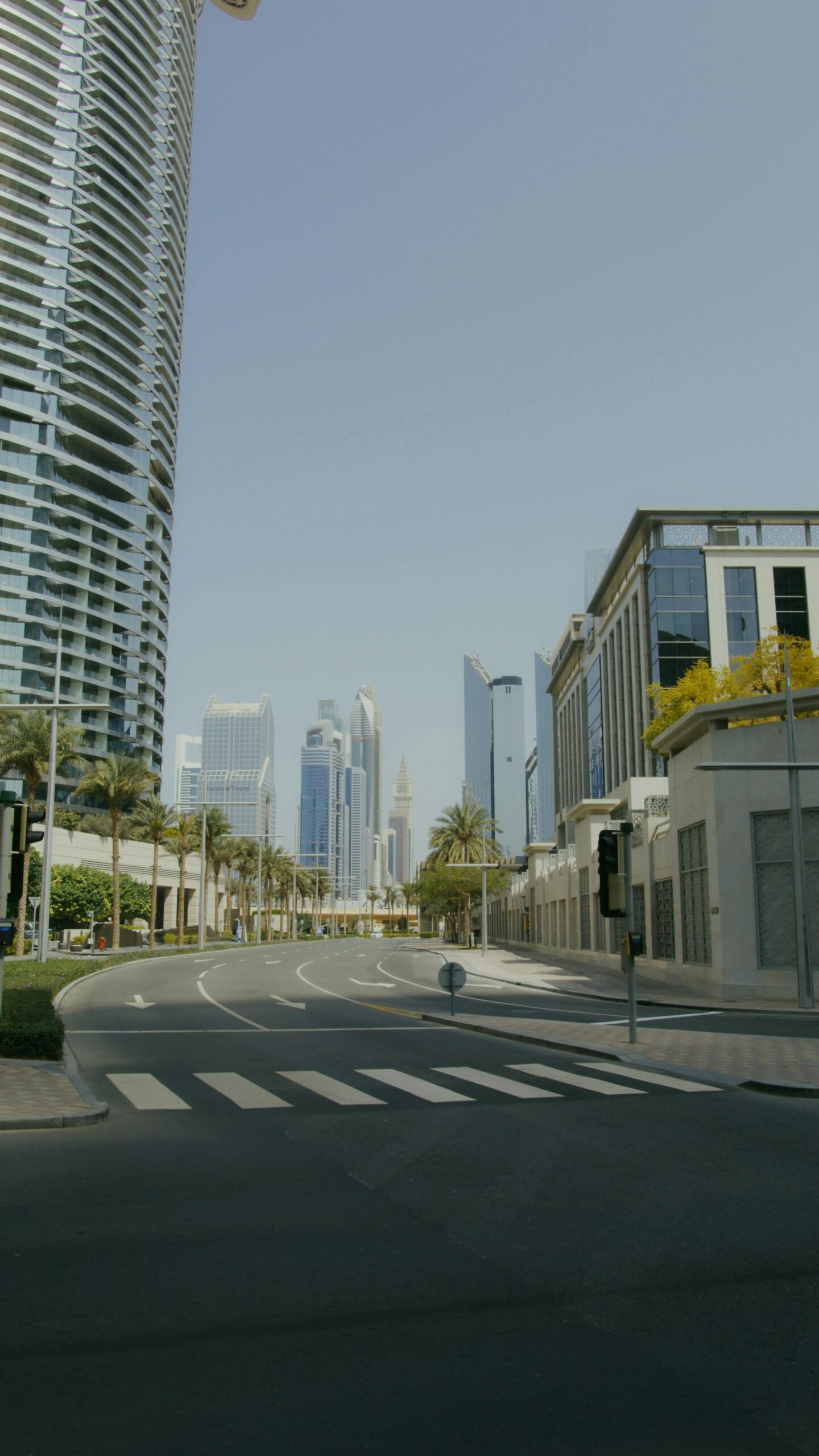 An empty road in a modern cityscape framed by towering skyscrapers under a clear sky.