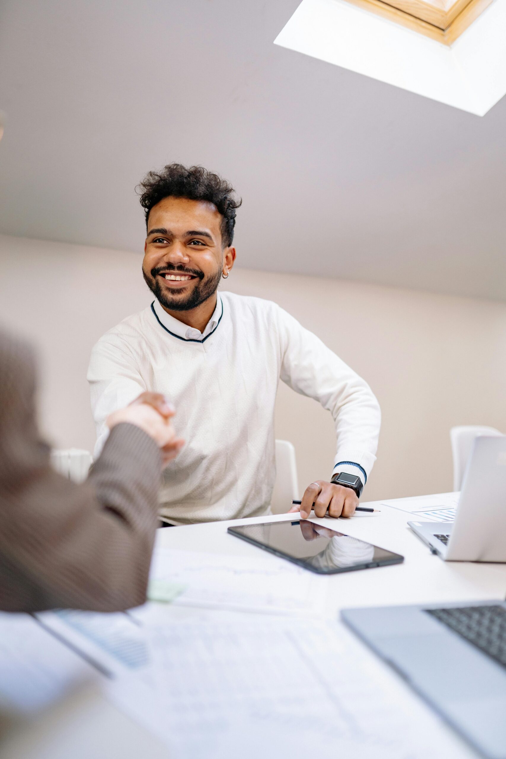 A smiling man in business attire shakes hands across a desk in a modern office.